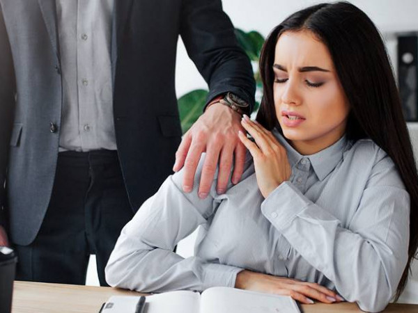  Concept harassment. Afraid young woman sit at table. Harrasment goes out of her boss. He keep hand on her shoulder. Guy wat to have sex with model